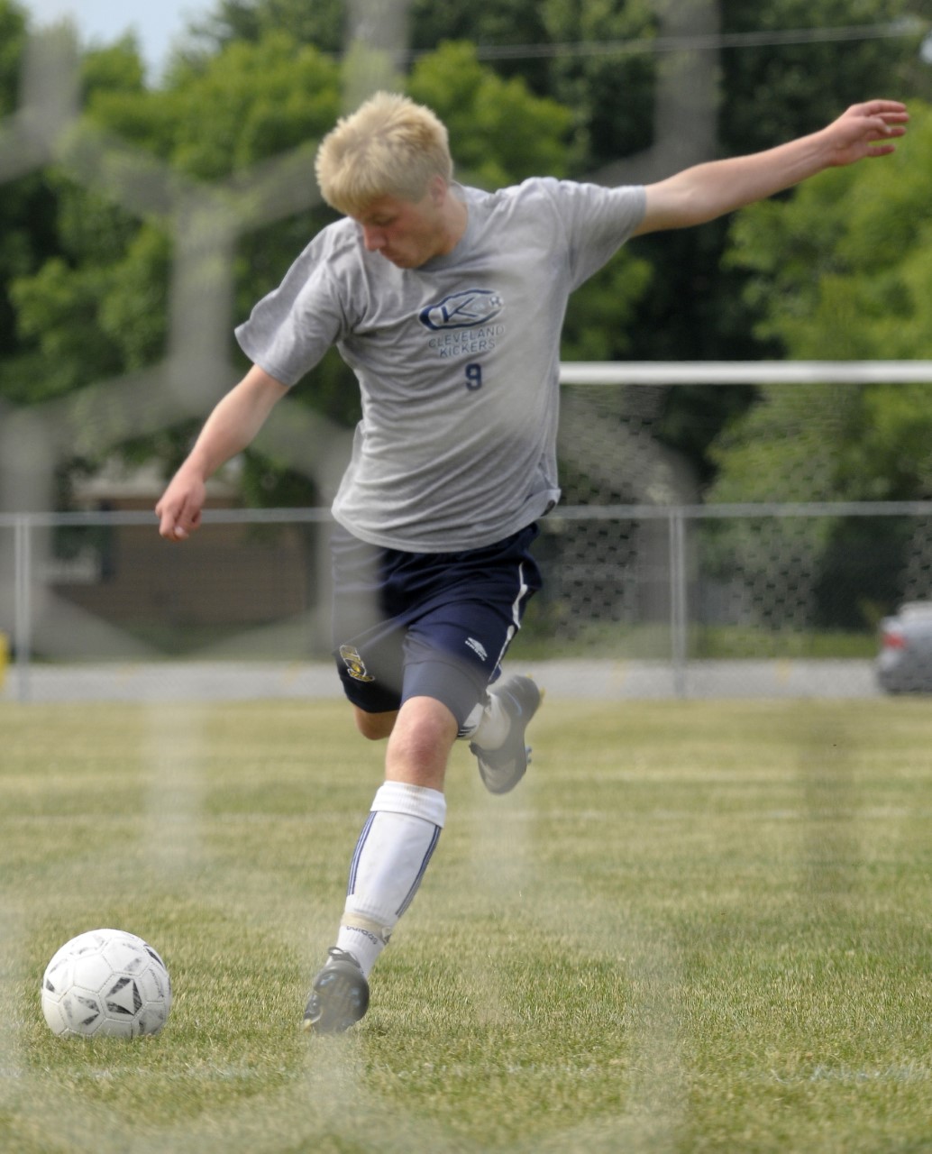 A high-school age boy strikes a shot towards goal