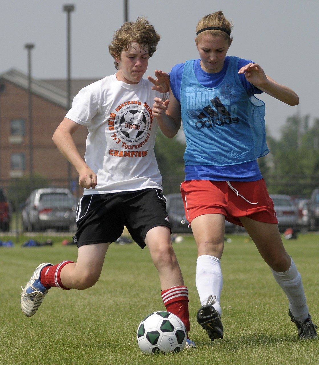 Two high school age soccer players, a male and female, challenge for the ball